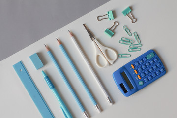 Stationary school supplies in white and blue tone, Scissors, pencils, paper clips,calculator, notepad  on blue and white background, Flat lay.