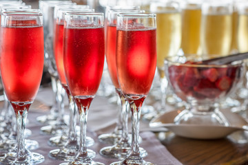 Close up of group of champagne glasses with pink and white champagne and a bowl of strawberries.