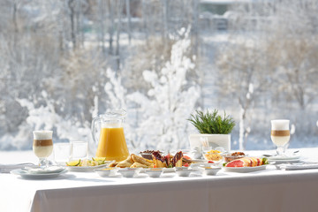 Winter Breakfast pancakes on the terrace outside the restaurant on the background of snow. Pancakes, fruit, juice, and coffee