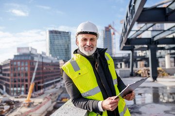 Man engineer standing outdoors on construction site, looking at camera.