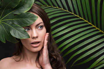Portrait of a young beautiful woman with perfect smooth skin with a large green tropical leaf