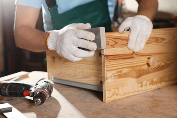 Professional carpenter polishing wooden drawer in workshop, closeup - obrazy, fototapety, plakaty