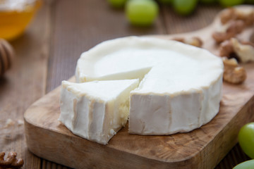 White, round cheeses on wooden background with honey and grapes. Dark food photo.