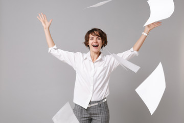 Cheerful joyful young business woman in white shirt posing isolated on grey background studio portrait. Achievement career wealth business concept. Mock up copy space. Throwing up papers documents.