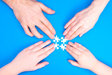 Hands of man, woman and children collect puzzle on a blue background background. Conceptual image of joint cooperation in the family. View from above