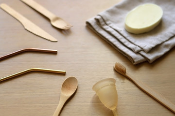 Various zero waste products on a wooden table: cloth, soap, cutlery, straws, toothbrush and menstrual cup. 