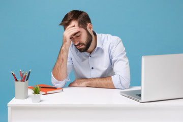 Tired sick young man in shirt sit work at desk with pc laptop isolated on blue background....