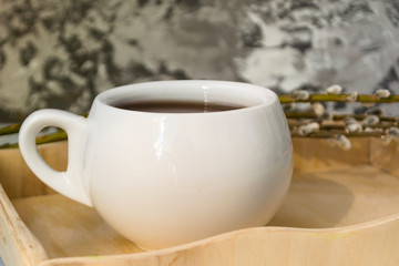 A willow twig with buds and a white cup of tea stands on a wooden tray. The concept of morning, breakfast