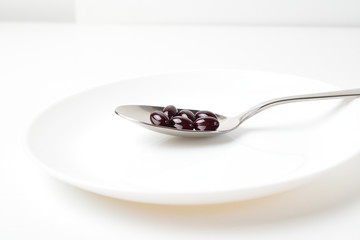 Astaxanthin capsules in the spoon on a white plate background. Side view.