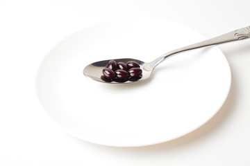 Astaxanthin capsules in the spoon on a white plate background.