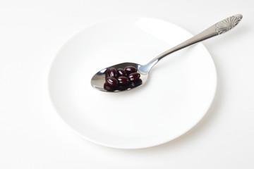Astaxanthin capsules in the spoon on a white plate background.