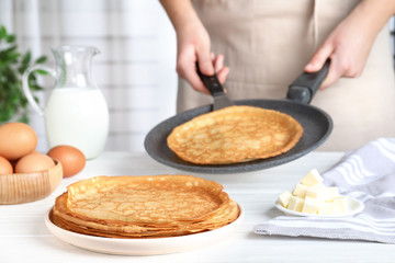 Woman cooking delicious thin pancakes at white wooden table