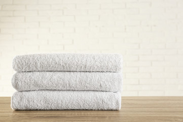 Obraz na płótnie Canvas Stack of clean bath towels on wooden table near white brick wall