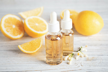 Bottles of citrus essential oil, flower and lemons on white wooden table