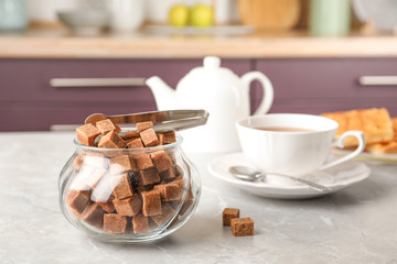 Glass bowl with brown sugar cubes and tongs on grey table