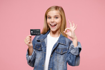 Funny little blonde kid girl 12-13 years old in denim jacket posing isolated on pastel pink wall...