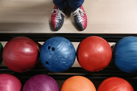 Person in bowling shoes near rack with balls, top view