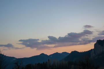Beautiful clouds against blue sky and silhouettes of mountain and trees, daytime in the forest