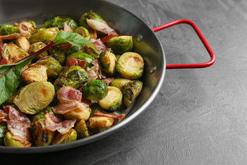 Delicious roasted Brussels sprouts with bacon in pan on black table, closeup