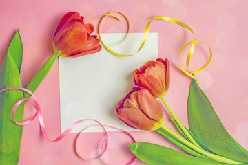 Mother's day background.Beautiful red tulips, multi-colored ribbons next to a sheet of white paper for text on a pink background. Save the space, top view. Greeting card for Women's Day, March 8