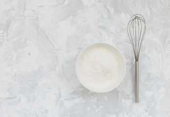 Flour bowl kitchen whisk on light white gray texture background.