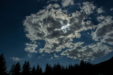 Beautiful clouds against blue sky and silhouettes of mountain and trees, daytime in the forest
