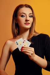 Blonde model with bright make-up, in black dress is showing two aces, posing against colorful background. Gambling, poker, casino. Close-up.