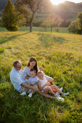 Young family with two small children sitting on meadow outdoors at sunset.