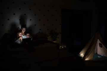 Fototapeta na wymiar Young mother with children sitting indoors in bedroom, using laptop.
