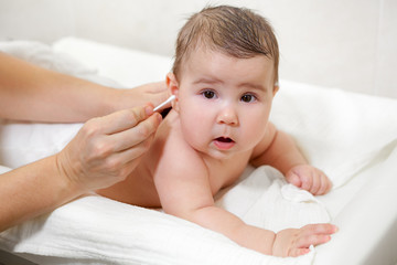 Female hands cleaning baby ears with cotton swab, infant hygiene after shower