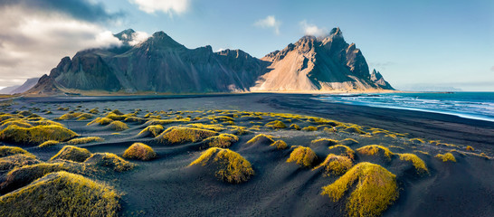 Blick von einer fliegenden Drohne. Atemberaubende Herbstszene von Stokksnes Cape mit Vestrahorn (Batman Mountain) im Hintergrund. Isländischer Panoramablick auf schwarze Sanddünen mit frischem grünem Gras. © Andrew Mayovskyy