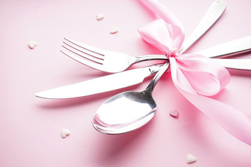 Sweet hearts and cutlery on a white plate with a pink ribbon on a pink background, flat lay. Valentine's Day. Mother's day background. Love concept.