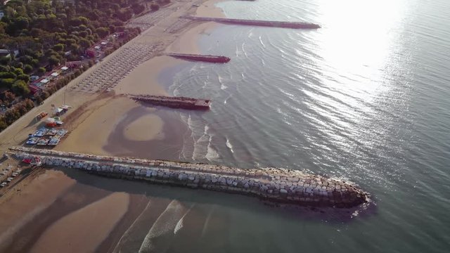 AERIAL: Looking down on the beautiful beach of Caorle, Italy. Sun reflects on the water.