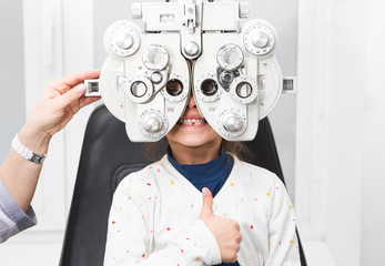 Girl shows thumb up at an ophthalmologist's appointment. Foropter - a device for measuring...