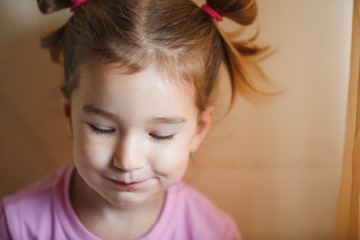Emotions of a cunning little girl of 3 years. A close-up girl with two light tails on her head is...