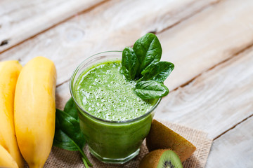 Healthy food and vegan diet concept - glass of fresh green juice or smoothie with kiwi, spinach, banana, apple. Antioxidant detox beverage, raw ingredients.  Close up, wooden background, copy space