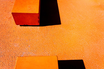 Asphalt floor painted in orange, with concrete blocks of harsh shadows of sunlight, abstract background.