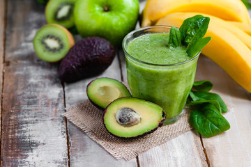 Healthy food and vegan diet concept - glass of fresh green juice or smoothie with kiwi, spinach, banana, avocado, apple. Antioxidant detox beverage with raw ingredients.  Close up, wooden background.