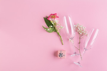 A bouquet of pink and white flowers, a small gift box and two glasses for sparkling wine on a pink...