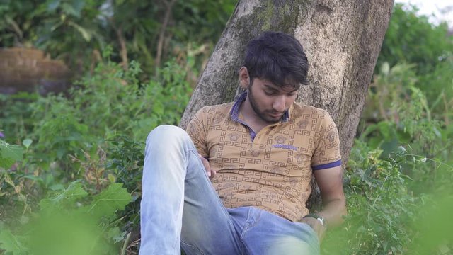 A drunk man sitting below a tree.Drunk Indian man looking tired. A drunk addicted Indian Man. Bad habit & bad addiction. Unhealthy person taking drugs, weed.