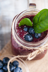 Healthy food and vegan diet concept - mason jar of juice or smoothie with blueberry, spinach, banana, kiwi, almond milk. Tasty detox beverage with raw ingredients.  Wooden background, close up, macro