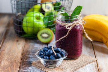 Healthy food and vegan diet concept - mason jar of juice or smoothie with blueberry, spinach, banana, kiwi, almond milk. Tasty detox beverage with raw ingredients.  Wooden background, close up, macro
