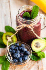 Healthy food and vegan diet concept - mason jar with smoothie with blueberry, spinach, banana, kiwi, almond milk. Detox beverage with raw ingredients.  Wooden background, close up, macro