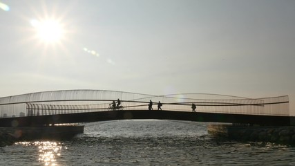 Silhouette of walking and riding bicycle people over the pedestrian bridge.