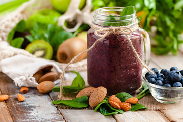 Healthy food and vegan diet concept - mason jar of fresh juice or smoothie with blueberry, spinach, banana, almond milk. Antioxidant detox beverage with raw ingredients.  Close up, wooden background.