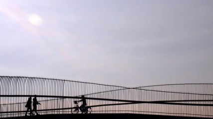 Silhouette of riding bicycle woman and couple walking over the bridge.