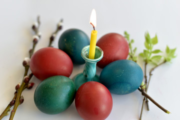 Easter eggs of different colors lie around a lit candle.