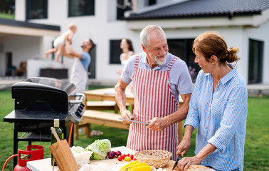 Senior couple with family outdoors on garden barbecue, grilling.