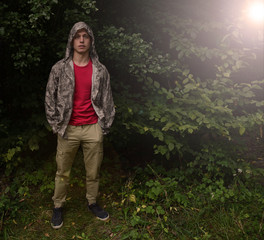 A young man in camouflage is standing in the forest and the sun is shining.