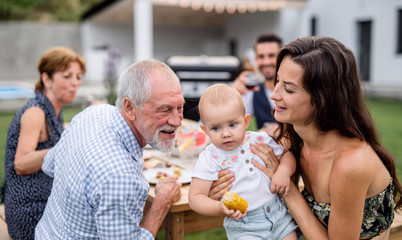 Portrait of extended family sitting at table outdoors on garden barbecue.
